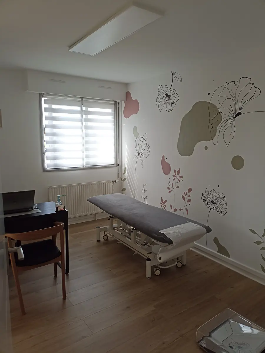 La salle de bilan: table d'examen grise, fresque de fleurs au trait noir, le podoscope en verre posé au sol.